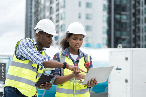 Group of African American engineer working in sewer pipes area at construction site. Male engineer and woman engineer discussing for maintenance sewer pipes, water tank on rooftop of building