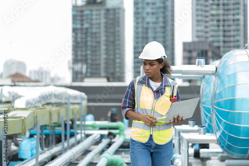 Female engineer working with laptop computer for checks or maintenance in sewer pipes area at construction site. African American woman engineer working in sewer pipes area at rooftop of building