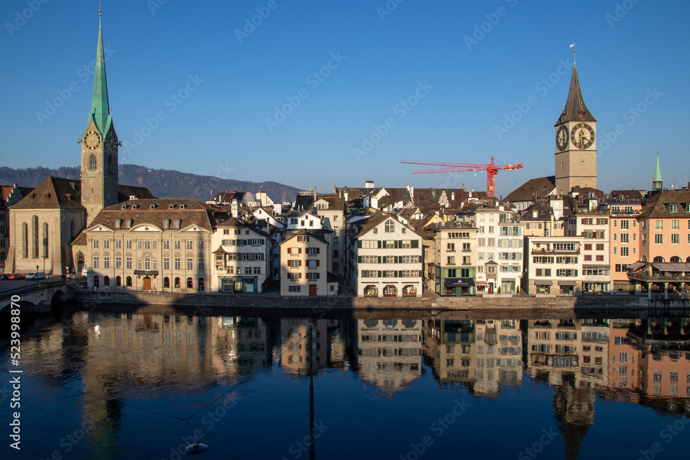 Altstadt in Zürich, Blick auf die Kirchen St. Peter und Fraumünster über der Limmat, Spiegelungen im Sonnenlicht am Morgen