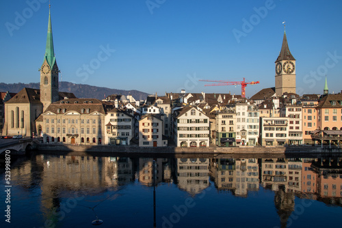 Altstadt in Zürich, Blick auf die Kirchen St. Peter und Fraumünster über der Limmat, Spiegelungen im Sonnenlicht am Morgen © M_Eidenbenz