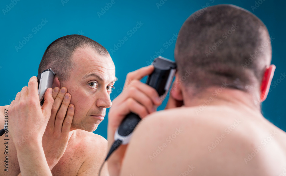 The man is cutting hair himself with a hair trimmer. The man is cutting hair himself with a hair trimmer.