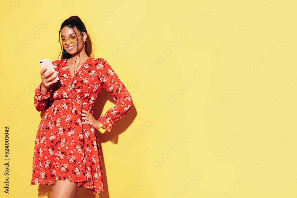 Young beautiful smiling female in trendy summer dress clothes. Sexy carefree woman posing near yellow wall in studio. Positive model having using phone apps. Holding smartphone, looking at screen Young beautiful smiling female in trendy summer dress clothes. Sexy carefree woman posing near yellow wall in studio. Positive model having using phone apps. Holding smartphone, looking at screen