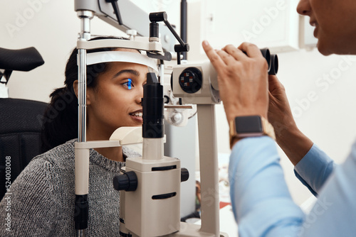 Eye test, exam or screening with an ophthalmoscope and an optometrist or optician in the optometry industry. Young woman getting her eyes tested for prescription glasses or contact lenses for vision photo