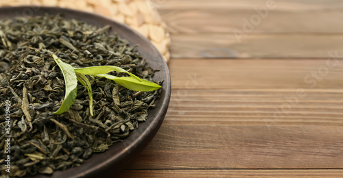 Plate with dry tea leaves on wooden table, closeup