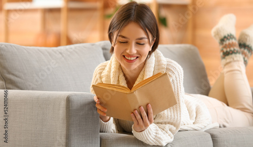 Happy young woman reading book on sofa at home