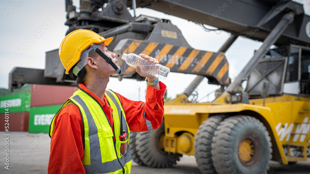 Foreman or worker is drinking a bottle of water after finishing work and relaxing on the old truck at cargo container port Foreman or worker is drinking a bottle of water after finishing work and relaxing on the old truck at cargo container port