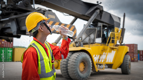 Foreman or worker is drinking a bottle of water after finishing work and relaxing on the old truck at cargo container port