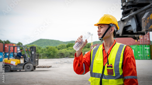 Foreman or worker is drinking a bottle of water after finishing work and relaxing on the old truck at cargo container port