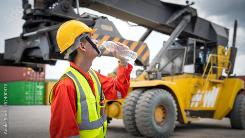 Foreman or worker is drinking a bottle of water after finishing work and relaxing on the old truck at cargo container port