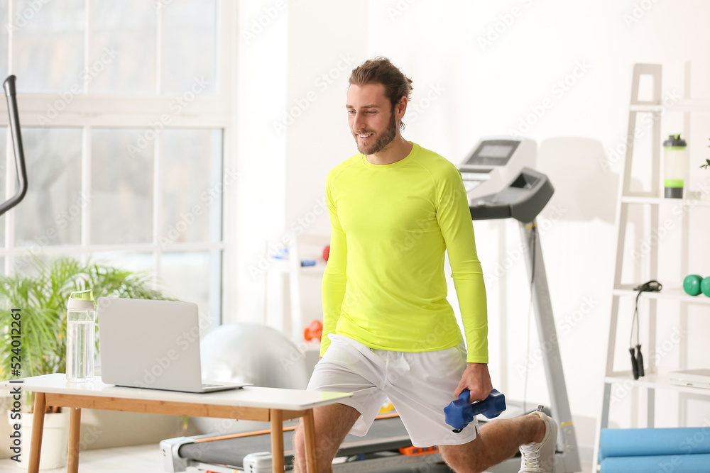 Fototapeta premium Sporty young man using laptop for online training in gym
