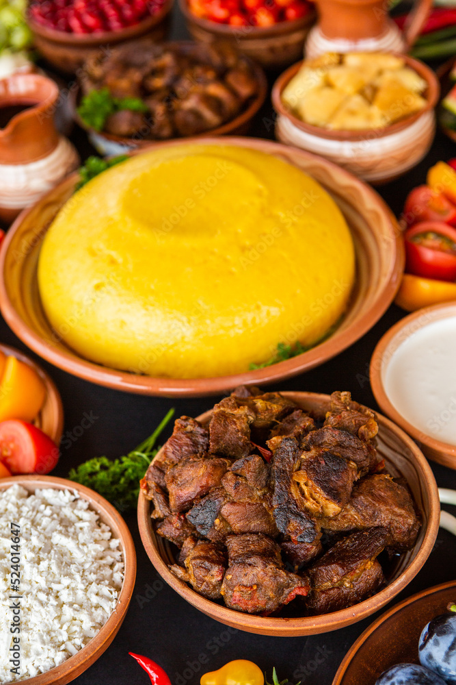 Homemade Romanian Food with polenta, meat, cheese and vegetables. Delicious corn porridge in clay dishes. Mamaliga or polenta, a traditional dish in Moldova, Hungary and Ukrainian cuisine.

