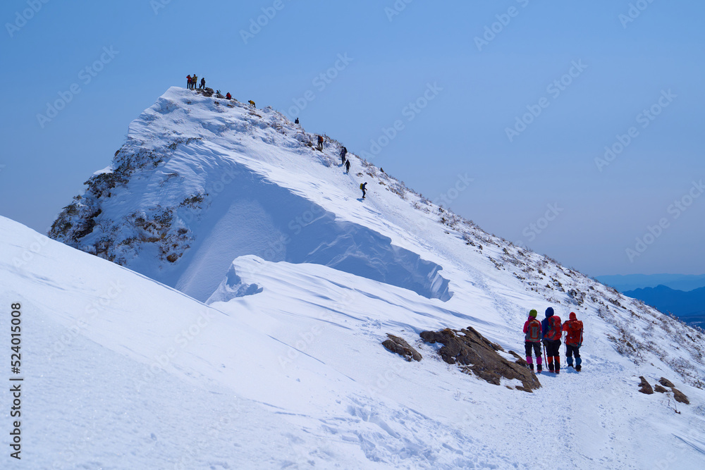 冬の谷川岳オキノ耳付近からトマノ耳山頂方面を見上げる女性登山者