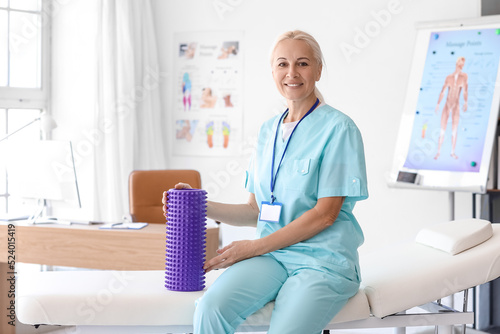Mature physiotherapist with foam roller sitting on couch in rehabilitation center