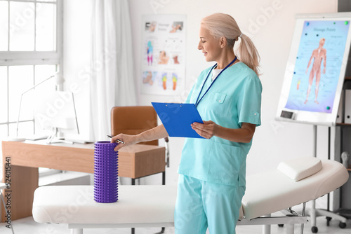 Mature physiotherapist with clipboard and foam roller in rehabilitation center