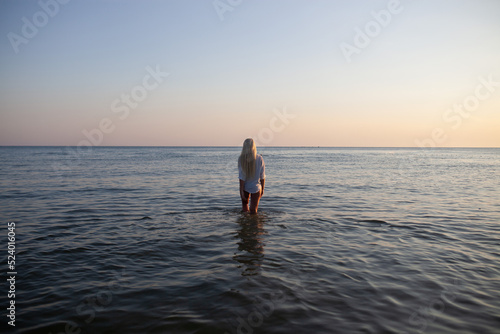 Girl in a shirt enters the water at sunset