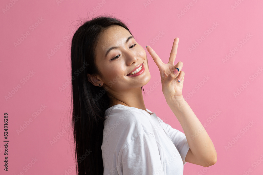 Portrait of asian positive smiling woman with V fingers gesture on pink background. Portrait of asian positive smiling woman with V fingers gesture on pink background.