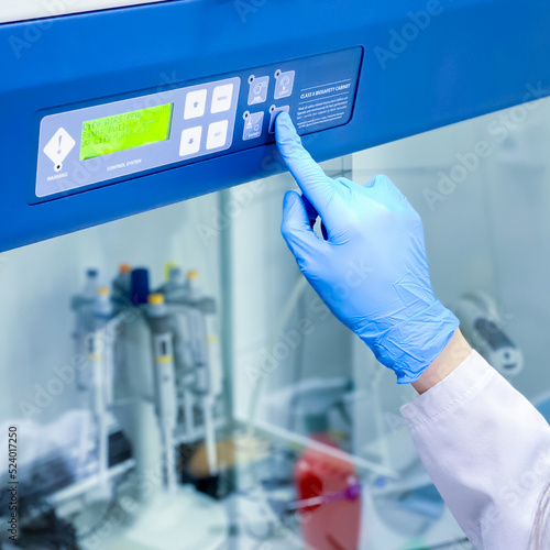 A researcher is turning on the safety laminar flow cabinet in a cell culture laboratory in order to initiate a work with deadly human virus. The cabinet provides sterile environment for such work.
