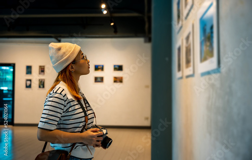 Fotografia Asian woman hold camera at art gallery collection in front framed paintings pict