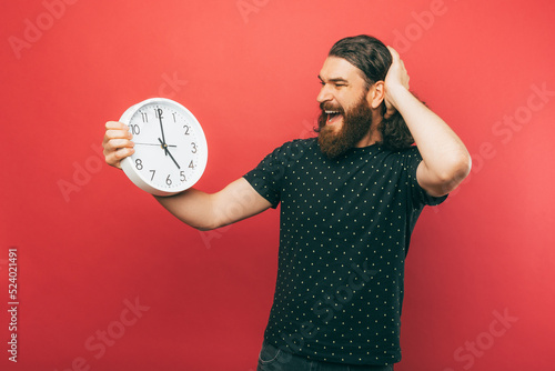 A photo of a an excited bearded man holding a white clock