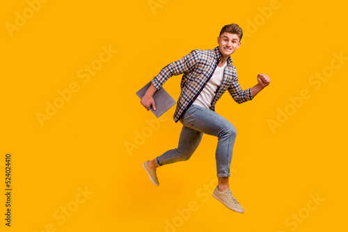 Full body profile side photo of young man jumper runnner rush hold laptop isolated over yellow color background