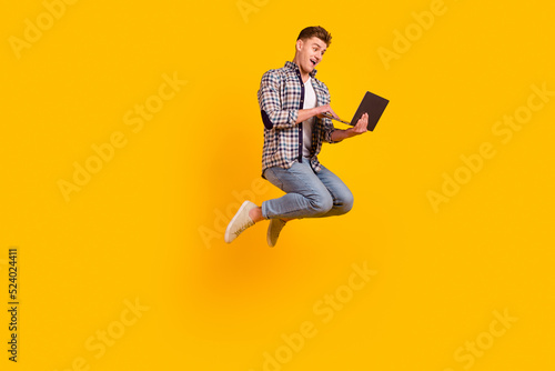 Full length profile side photo of young man jump up use laptop representative isolated over yellow color background