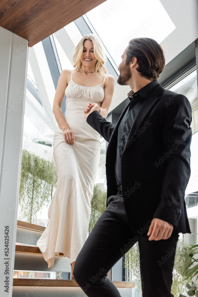 Elegant man in suit holding hand of girlfriend in dress on stairs in restaurant. Elegant man in suit holding hand of girlfriend in dress on stairs in restaurant.