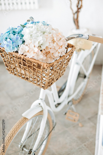 Vintage white bicycle with flowers in a basket against a white wall. Selective focus