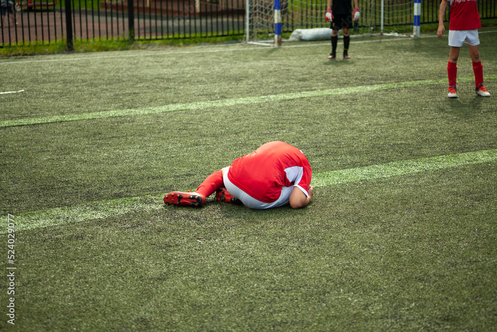 Obraz premium Footballer fell. Child plays football. Injury on field. Game details.