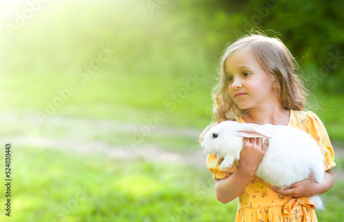 a little girl with a white rabbit in her hands is looking towards the sun's rays
