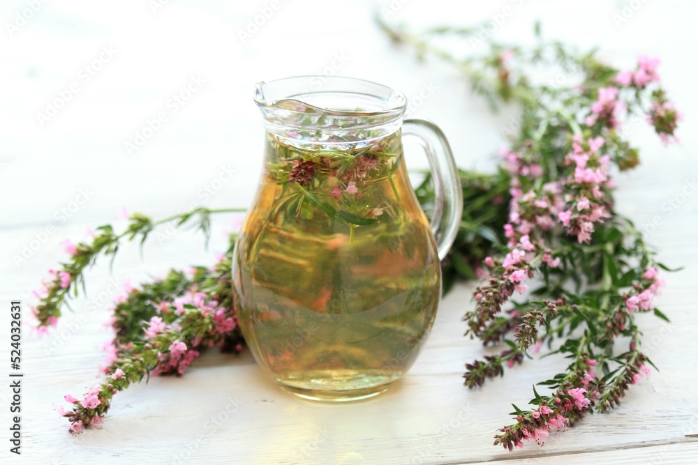 Herbal tea in glass with fresh flowers of hyssopus, lat. Hyssopus officinalis. Homemade tea from hyssopus and hot water in a jug on white wooden table. Herbal tea in glass with fresh flowers of hyssopus, lat. Hyssopus officinalis. Homemade tea from hyssopus and hot water in a jug on white wooden table.