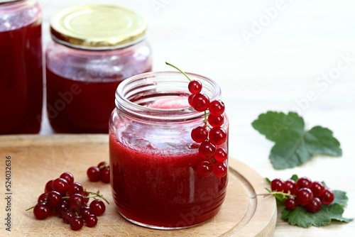 Homemade preserved red currant jam in jars. Red currants and preserved jars on white wooden table.