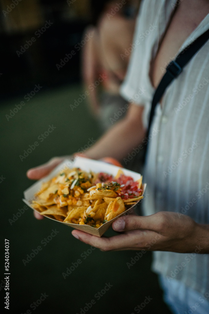 Close-up view of the hands of a festival goer with a serving of potatoes bought from a food truck