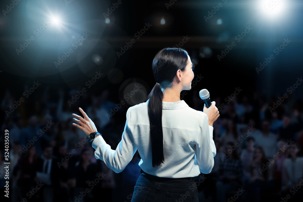 Motivational speaker with microphone performing on stage, back view