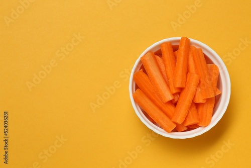 Cut fresh carrot in bowl and space for text on orange background, top view. Finger food photo