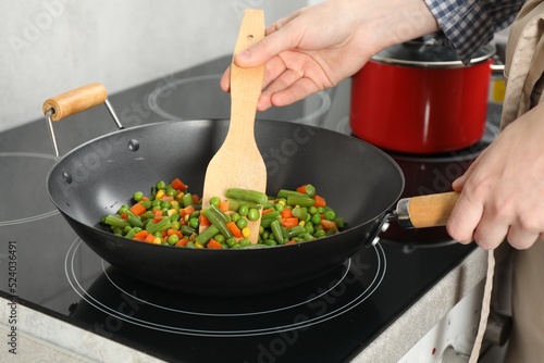 Woman cooking tasty vegetable mix in wok pan at home, closeup