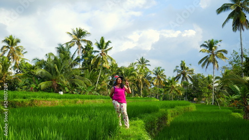 charmante Balinesin steht im grünem Reisfeld in Bali umgeben von vielen Palmen und schönem Himmel