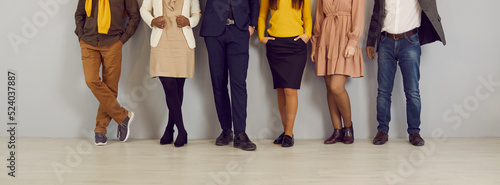 People in smart casual clothes by office wall. Row of company employees in pants, skirts, jackets and jumpers of brown, yellow, dark blue, beige color. Low section legs. Work dress code concept header