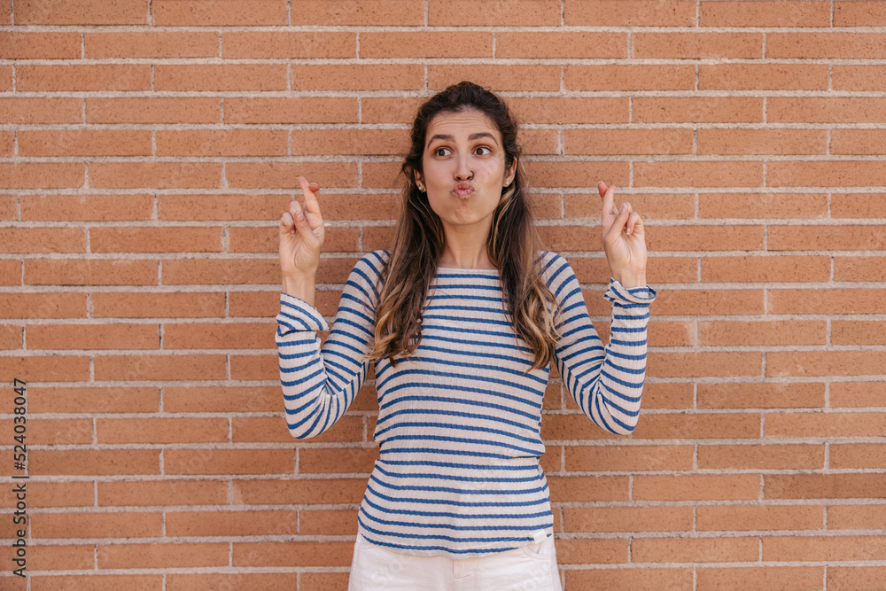 Funny young caucasian woman with pouted lips crosses her fingers standing near city wall. Brown-haired girl looks away, wears sweatshirt in spring. Lifestyle concept Funny young caucasian woman with pouted lips crosses her fingers standing near city wall. Brown-haired girl looks away, wears sweatshirt in spring. Lifestyle concept