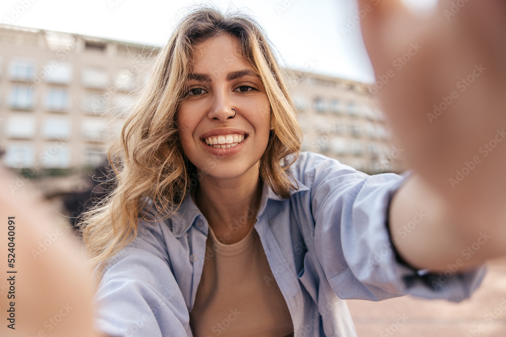 Pretty young caucasian woman with piercing smiles broadly relaxing outdoors. Blonde wears casual clothes. Relaxed lifestyle, concept.