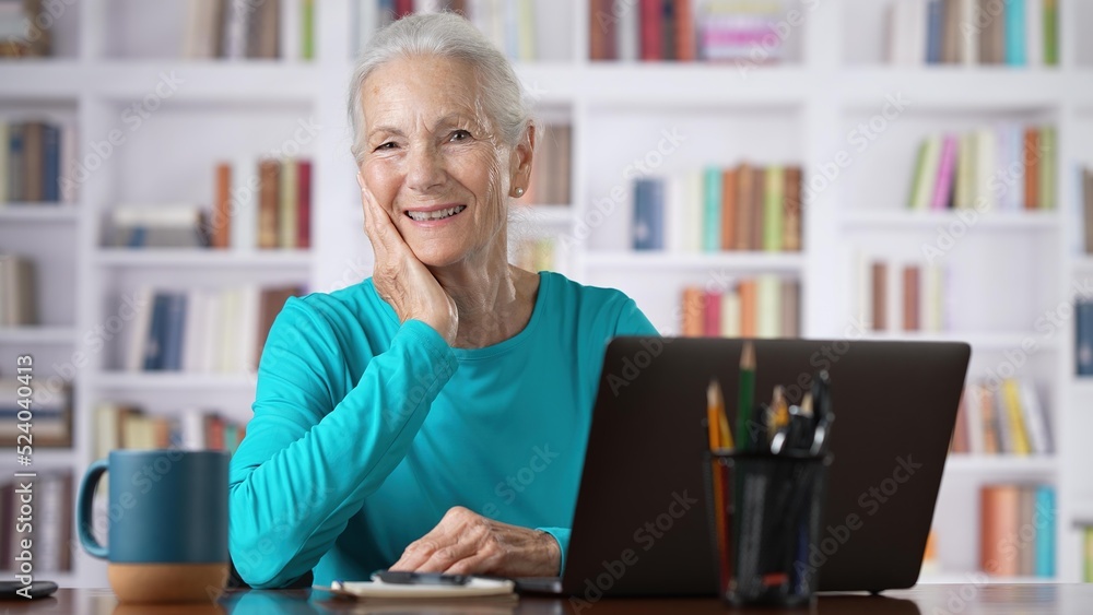 Portrait of elderly senior older woman on laptop looks up and smiles online concept, watching business training class, live webinar on laptop computer remote working, distance learning, home office. Portrait of elderly senior older woman on laptop looks up and smiles online concept, watching business training class, live webinar on laptop computer remote working, distance learning, home office.