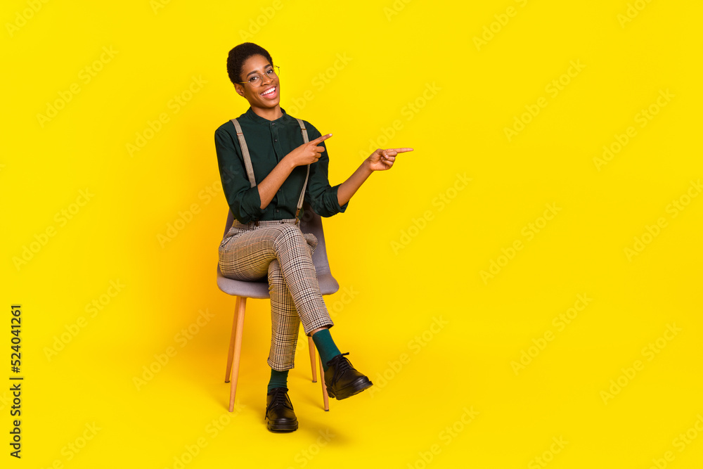 Full length body size view of attractive cheery woman sitting demonstrating copy space isolated over bright yellow color background Full length body size view of attractive cheery woman sitting demonstrating copy space isolated over bright yellow color background