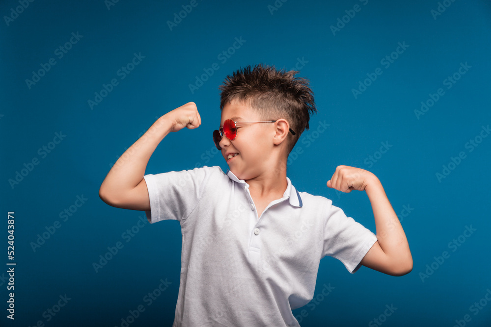 A confident guy shows his muscles. A sporty child is a boy demonstrating the strength of the biceps muscles of his arm. A schoolboy with glasses. A confident guy shows his muscles. A sporty child is a boy demonstrating the strength of the biceps muscles of his arm. A schoolboy with glasses.
