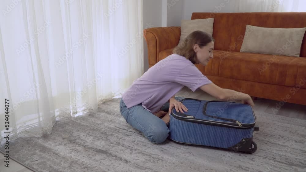 A woman closes a suitcase with clothes sitting on the floor, preparing for the trip A woman closes a suitcase with clothes sitting on the floor, preparing for the trip