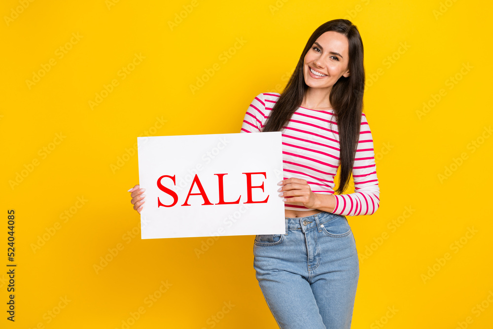 Portrait of young attractive cute smiling woman hold placard sale shopping clothes low price isolated on yellow color background Portrait of young attractive cute smiling woman hold placard sale shopping clothes low price isolated on yellow color background