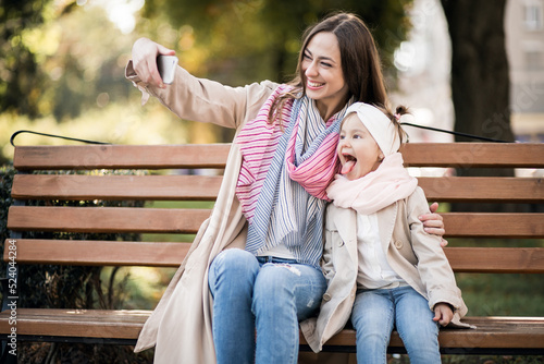 Mother with little daughter sitting on bench and making selfie