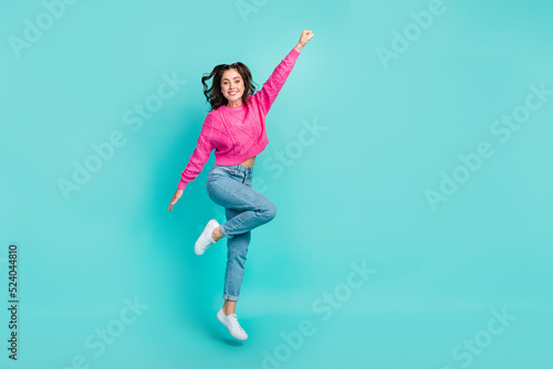 Full size photo of gorgeous cute woman with curly hairdo wear pink sweater jeans raise fist fliying isolated on turquoise color background