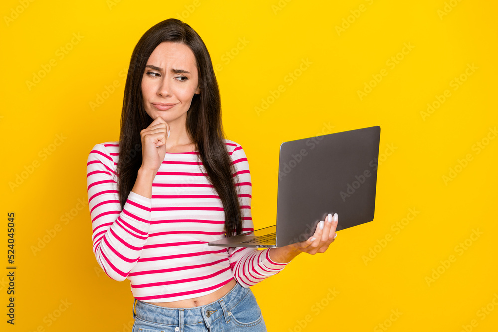 Photo of young attractive gorgeous minded girl touch chin thoughtful unsure look laptop isolated on yellow color background Photo of young attractive gorgeous minded girl touch chin thoughtful unsure look laptop isolated on yellow color background