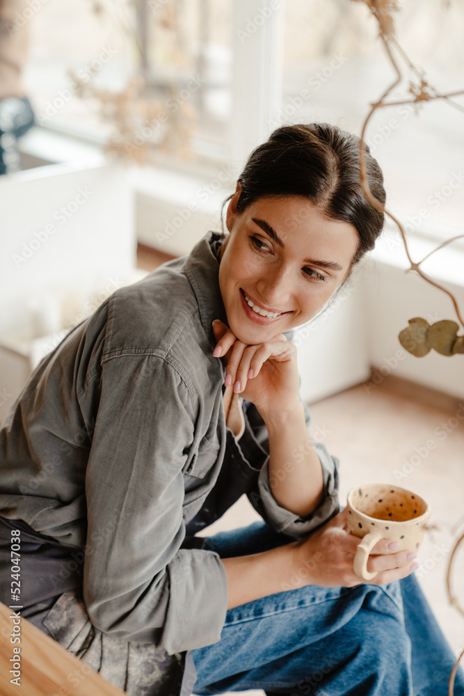 Side view of young beautiful calm woman holding clay cup Side view of young beautiful calm woman holding clay cup