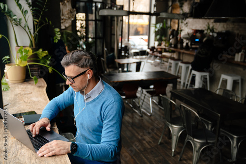 Adult focused man in glasses and headphones working with laptop