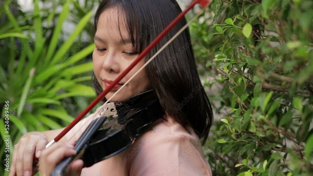 An Asian woman playing a classical instrument violin in the garden at home having fun and happiness. Band concept, classical music concert An Asian woman playing a classical instrument violin in the garden at home having fun and happiness. Band concept, classical music concert